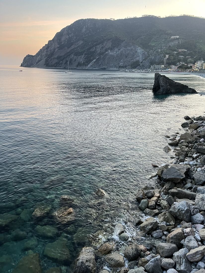 Clear water and a rocky shore below a headland at dusk