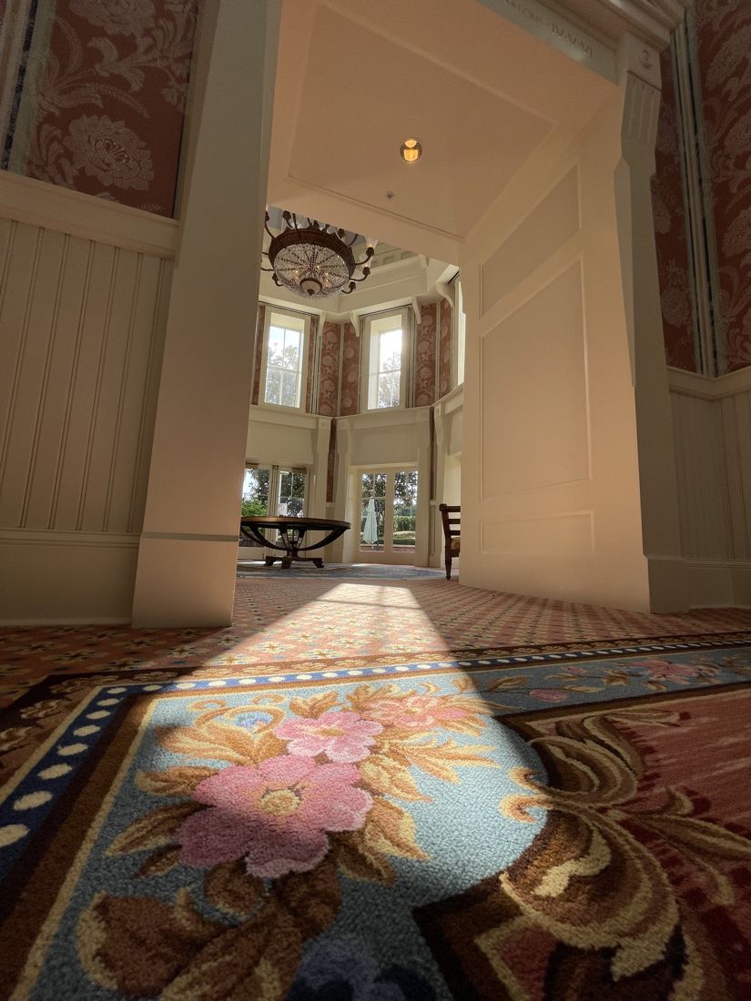 Low view across a floral carpet into a sunlit hall with a chandelier