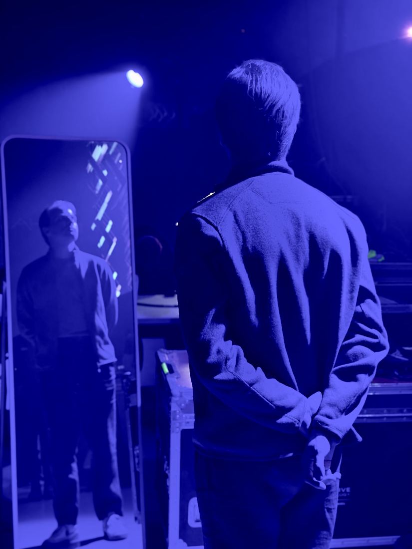 A man facing a mirror under blue stage light